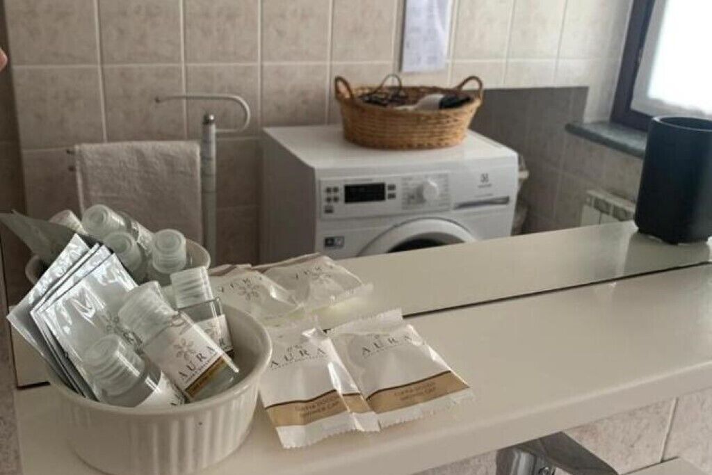 A bathroom with a white sink, a basket on the counter, and a washing machine in the background.