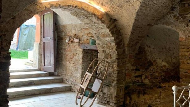 A stone-walled room with a wooden door, a small shelf with a green object, and a white chair. - Censo Guest House : are you ready for your next adventure? (Marsaglia)
