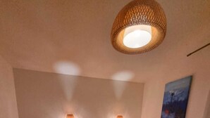 A bedroom with a bed, two bedside lamps, a painting on the wall, and a ceiling light fixture.
