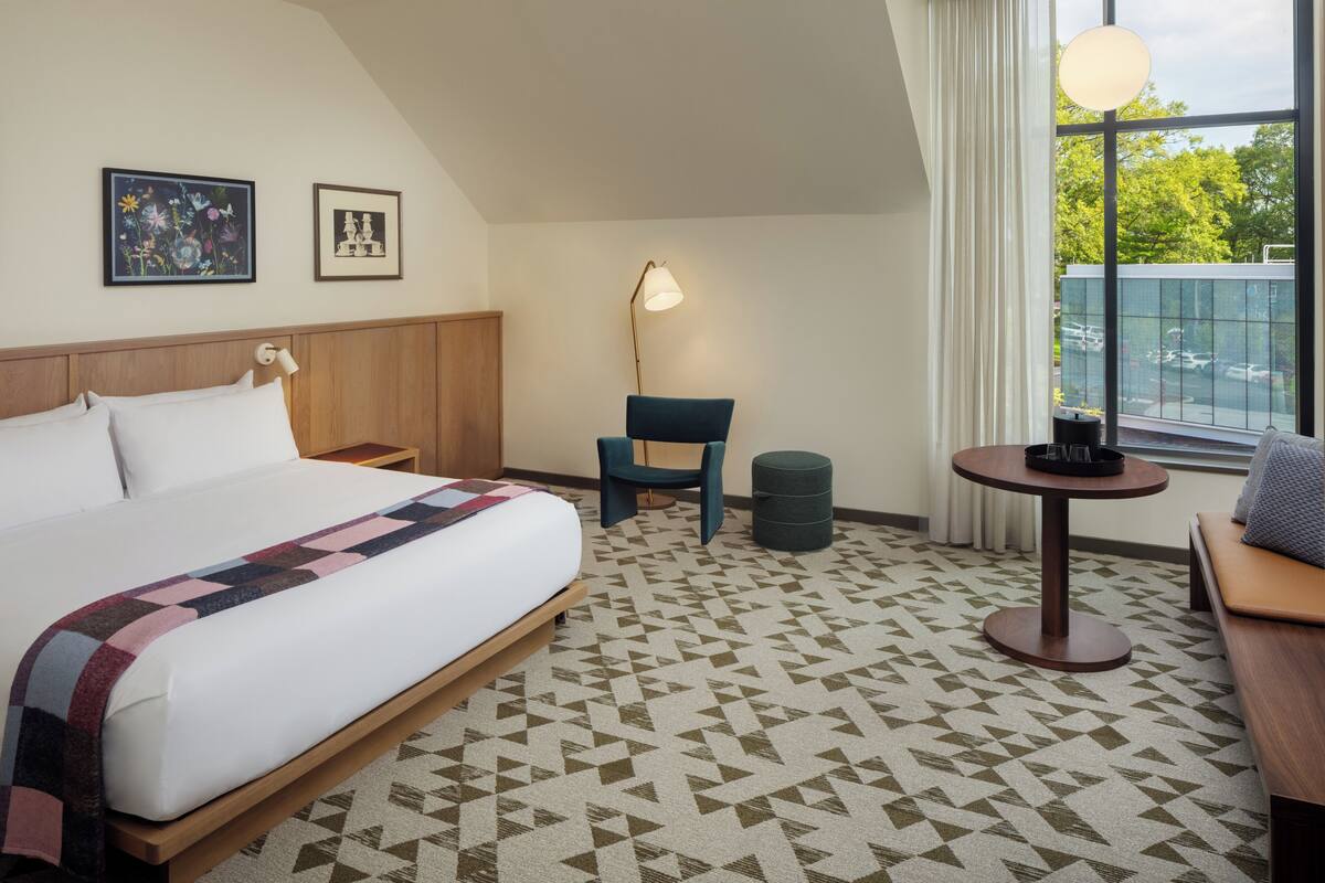 Habitació d'hotel amb un llit gran, una escriptori, una cadira, una taula rodona i vistes a l'exterior.