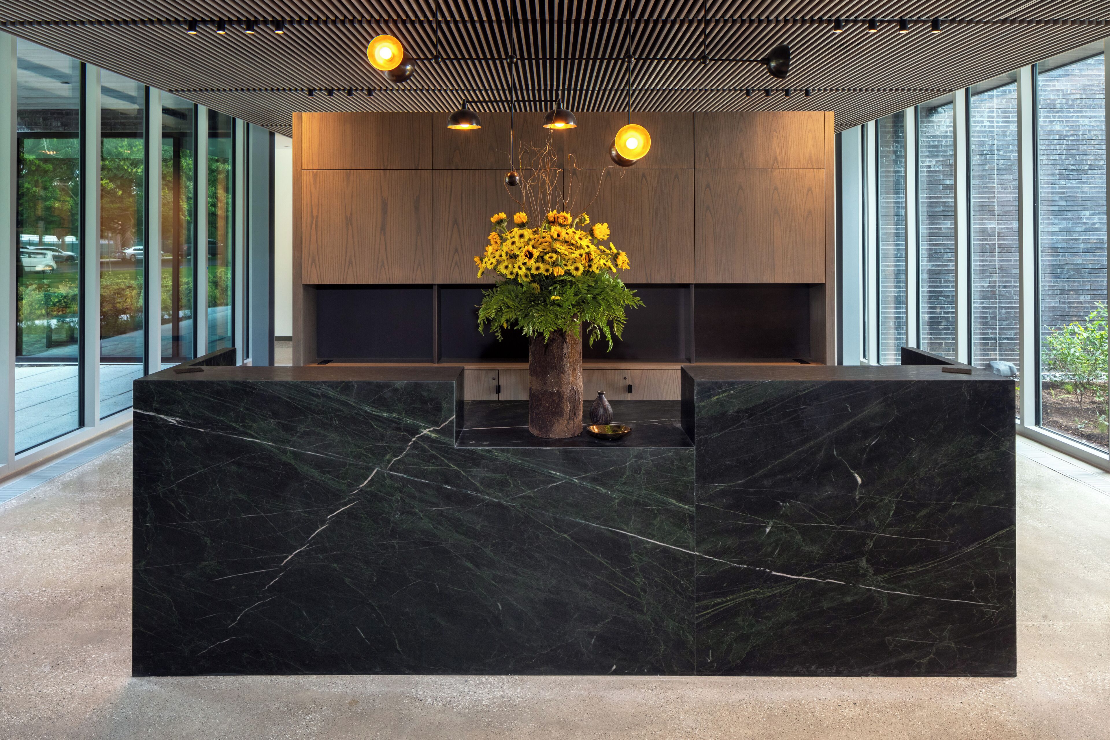 A modern reception desk with a marble top, a wooden cabinet, and a vase of sunflowers.