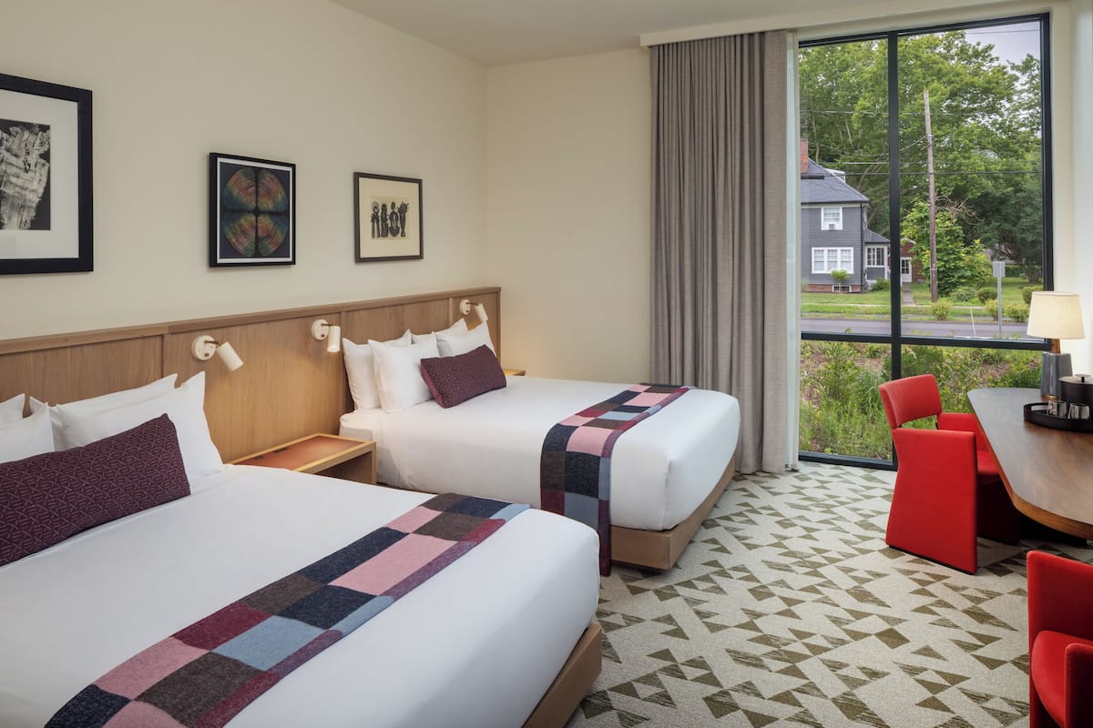 Habitació d'hotel amb dos llits, una zona de menjador i vista a un barri residencial.