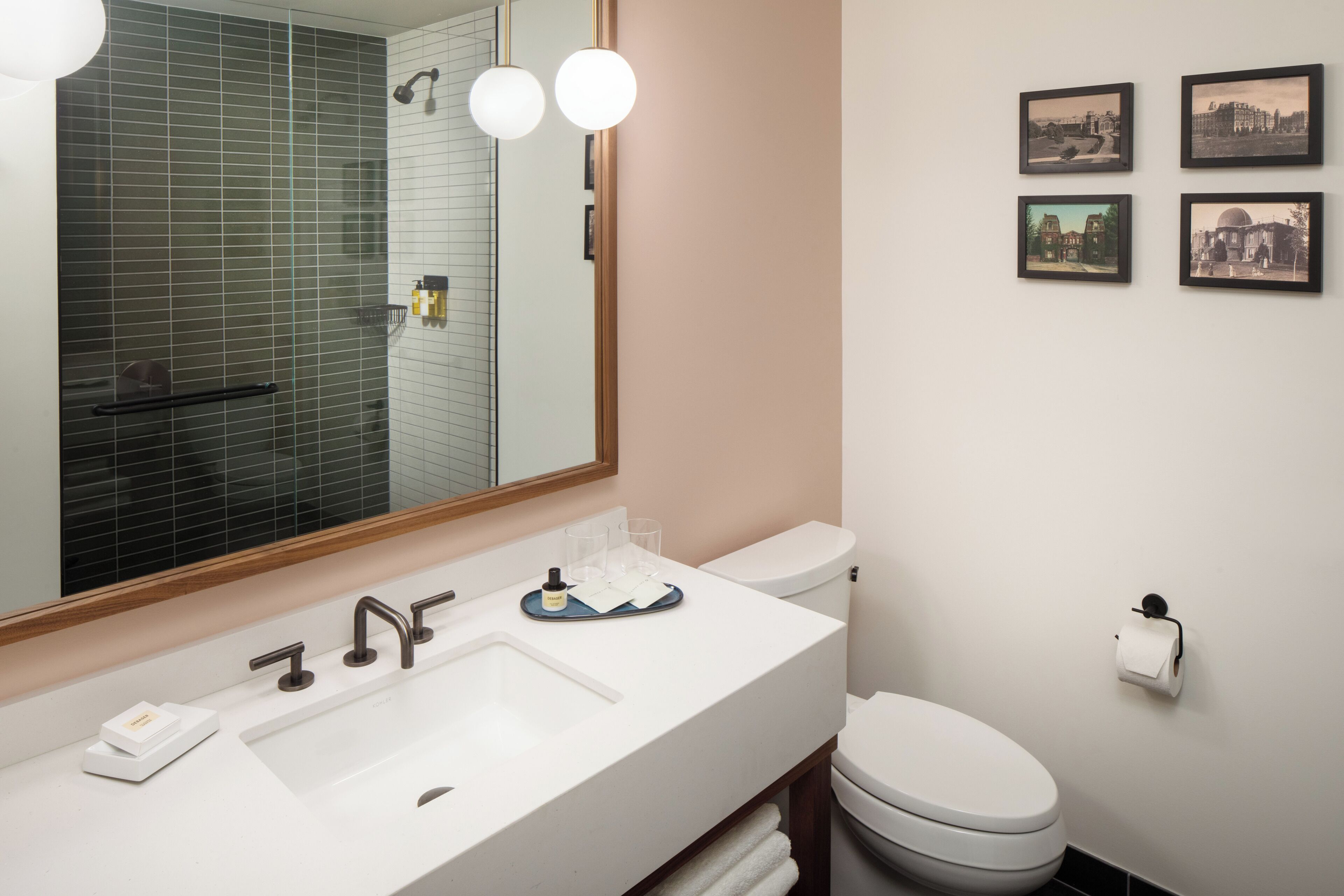 Un baño moderno con un espejo grande, un lavamanos blanco, un inodoro y cuatro cuadros enmarcados en la pared.