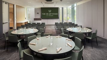 A conference room with multiple round tables, each set with glassware and napkins, and a large screen displaying "The Heartwood at Vassar".
