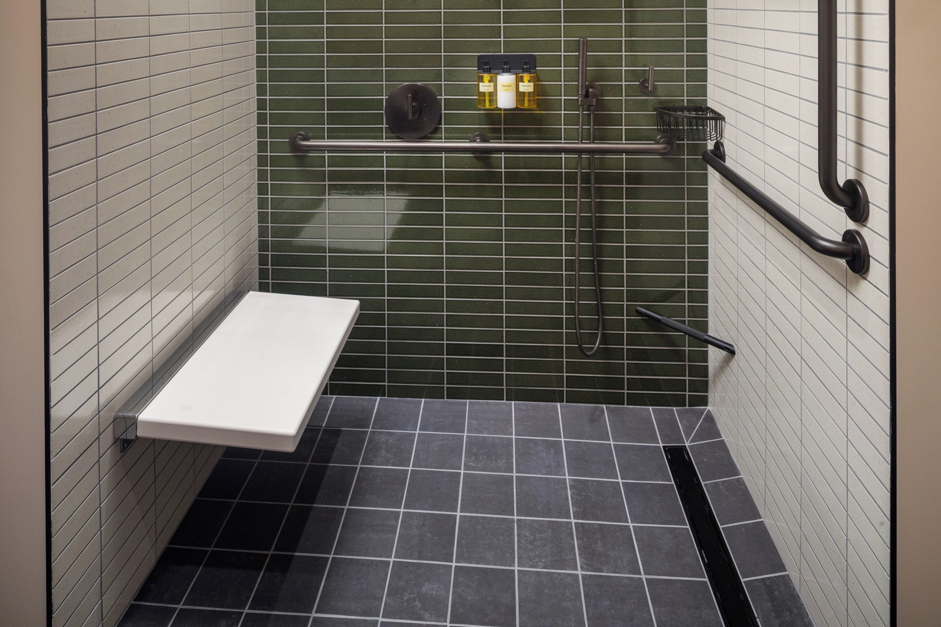 Ein kleines Badezimmer mit gefliesten Wänden, einem weißen Waschbecken, einer Dusche und einer Haltestange.