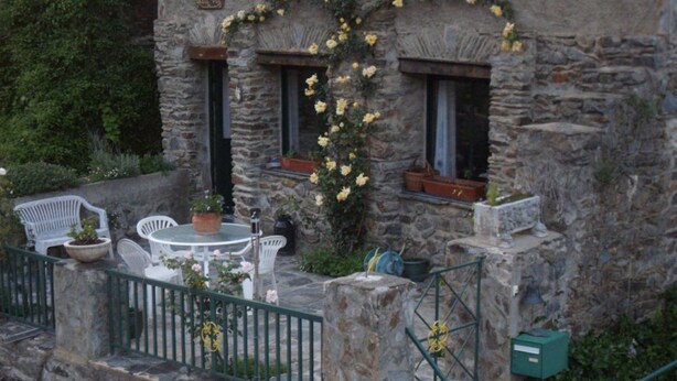 Edifici de pedra amb un balcó, zones d'estar a l'exterior i plantes en testos.