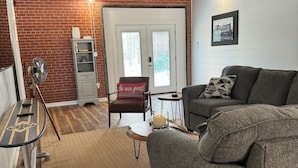 A cozy living room with a brick wall, a gray sofa, a small table, and a basket. - The Apalachicola Train Depot (Apalachicola)