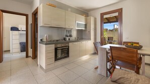 A modern kitchen with a built-in oven, a microwave, and a gas stove. There is a dining table with chairs and a window overlooking a garden. - 3844 Villetta Della Poesia by Barbarhouse (Melendugno)