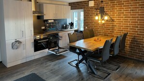 A modern kitchen with white cabinets, a wooden dining table, and a brick wall. - Ferienwohnung Deichgraf Direkt an den Oder- Auen (Schwedt/Oder)