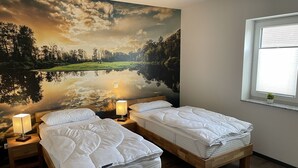 A bedroom with two beds, a large mural of a landscape, a window with blinds, and a small plant on the windowsill. - Ferienwohnung Deichgraf Direkt an den Oder- Auen (Schwedt/Oder)