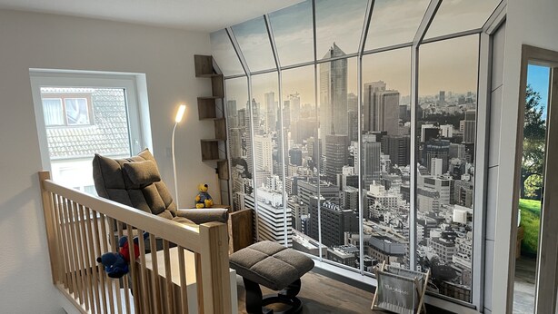 A modern room with a cityscape view, a wooden chair, a small table, and a plush toy. - Ferienwohnung Deichgraf Direkt an den Oder- Auen (Schwedt/Oder)