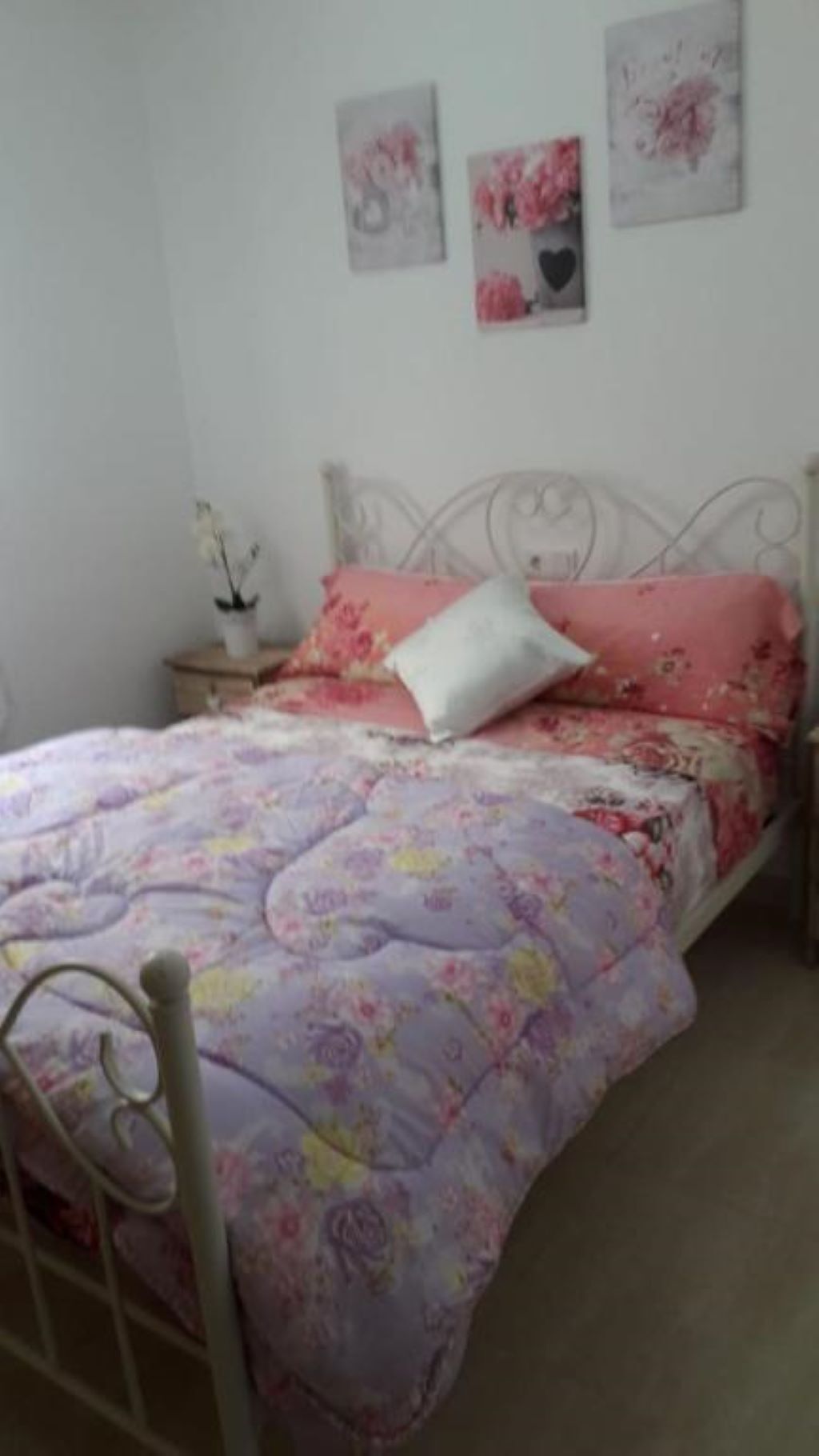 A bedroom with a floral bedspread, a white pillow, and two wall art pieces.