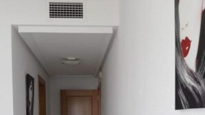 A narrow hallway with a wooden door at the end, a vent on the ceiling, and a painting on the wall. - El Campello Deborah. à 10 Minutes à Pied de la Plage et 5 Minutes du Centre (El Campello)