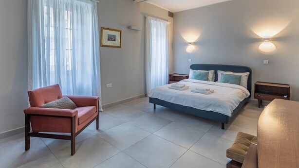 Un dormitorio con cama, una silla, una mesita de noche y una lámpara de pared.