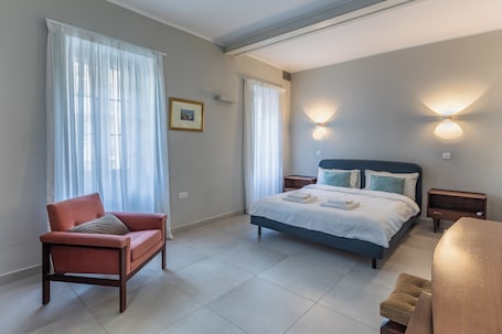 A bedroom with a bed, a chair, a bedside table, and a wall-mounted light fixture.