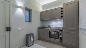 Cocina compacta con gabinetes grises, un bote de basura de acero inoxidable y ventana con vistas.
