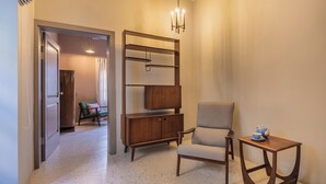 A modern living room with a wooden cabinet, a grey armchair, and a small table with a teapot. - Mid-Century Retro Suite (Floriana)