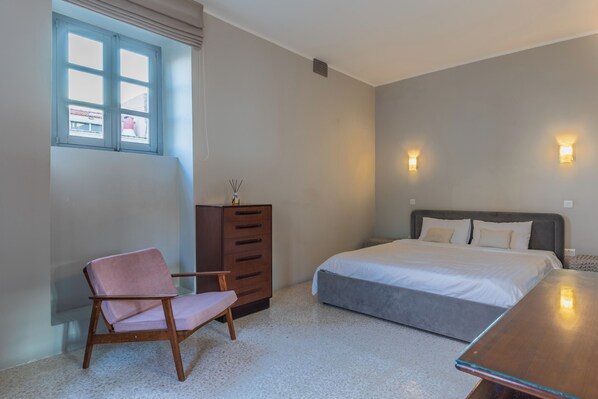 A bedroom with a bed, a chair, a dresser, and a window.