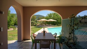 Un patio con mesa y sillas, piscina y vistas a una colina.