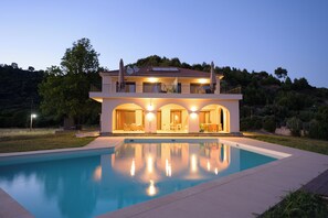 Una moderna casa a due piani con piscina di fronte, dotata di un balcone con mobili da esterno e vista sul paesaggio circostante.