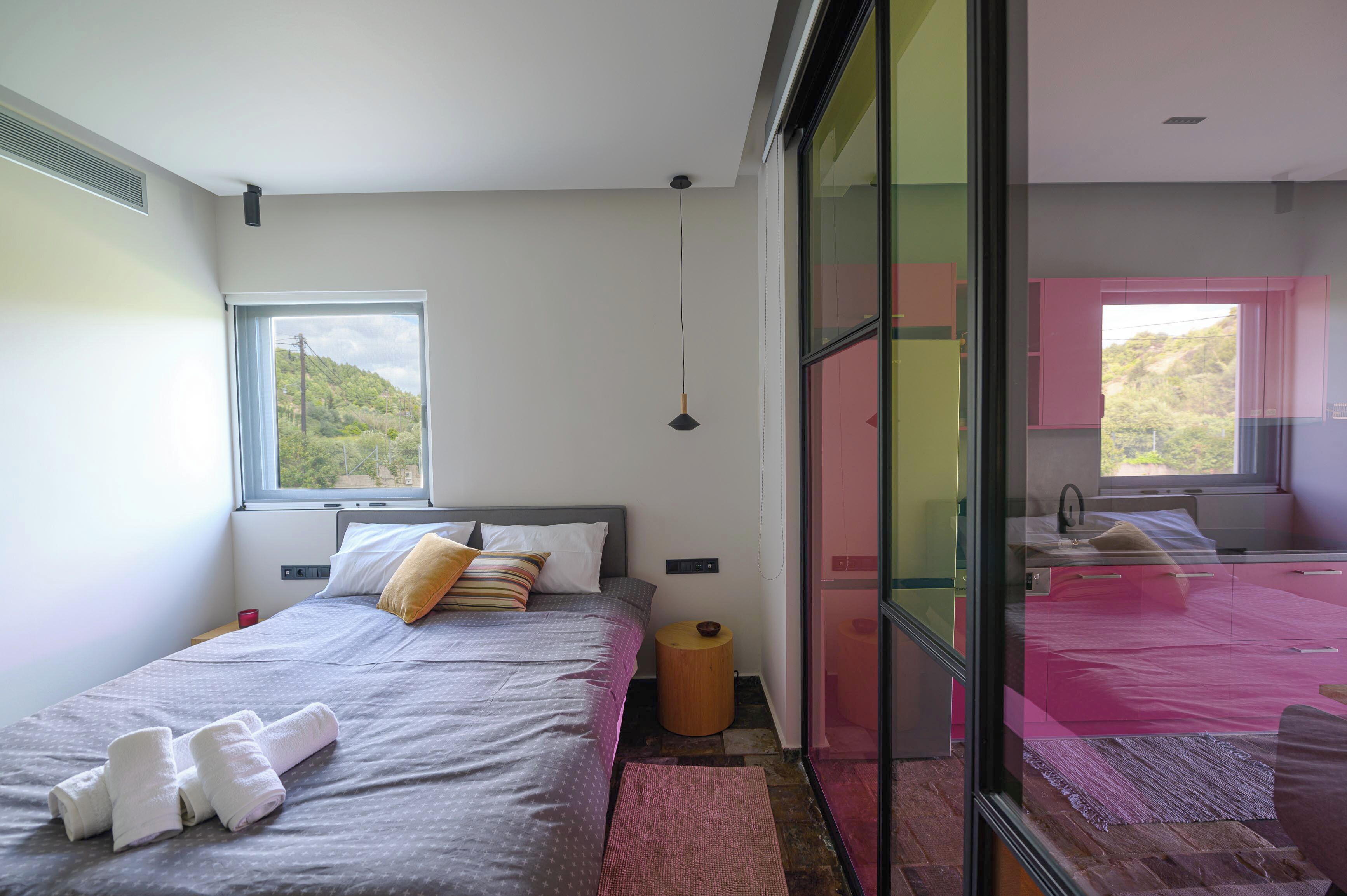 Una camera da letto moderna con un'ampia finestra, un letto con asciugamani ordinatamente piegati e un piccolo sgabello di legno.