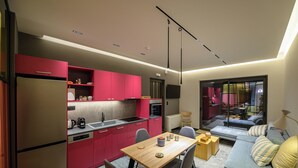 Una cocina moderna con armarios rojos, un comedor con mesa y sillas de madera, y una sala de estar con sofá y lámpara.
