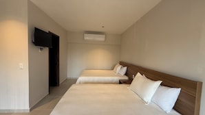 A hotel room with two beds, a TV mounted on the wall, and an air conditioning unit.