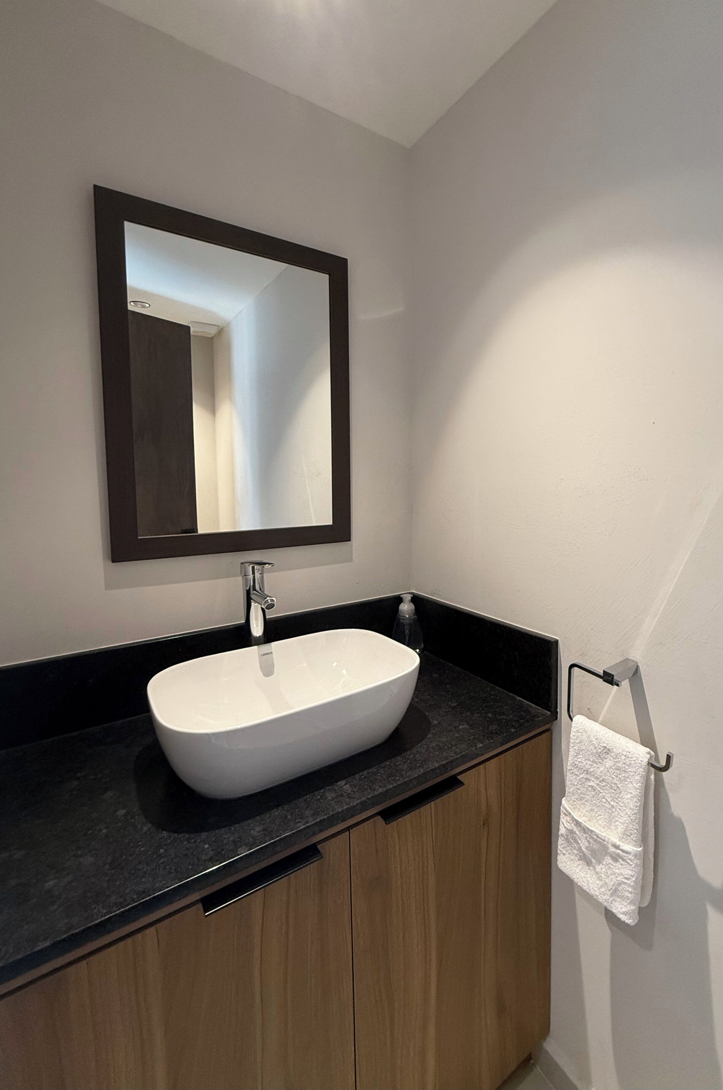 A bathroom with a white sink, dark countertop, and wooden cabinets.