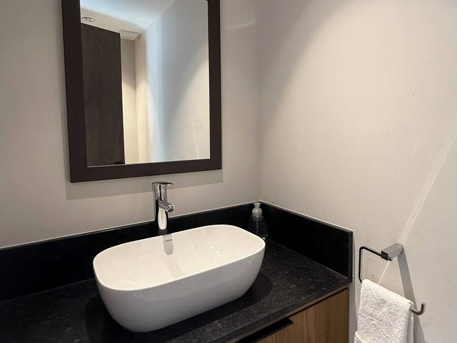 Un baño con lavamanos blanco, encimera oscura y armarios de madera.