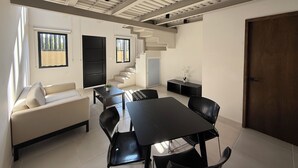 A modern living room with a sofa, dining table, chairs, a staircase, and a door.