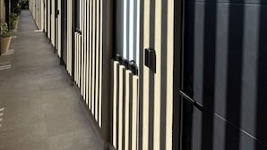A corridor with a series of doors and windows, a tiled floor, and a wall with vertical lines.