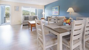 A dining area with a wooden table and white chairs, a sofa with patterned cushions, and a painting on the wall. - Atlantic Beach Getaway Spacious 3-Level Condo: Walk to the Beach & Pool (Atlantic Beach)
