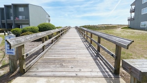 A wooden boardwalk leading to a building with balconies, surrounded by grass and bushes. - Atlantic Beach Getaway Spacious 3-Level Condo: Walk to the Beach & Pool (Atlantic Beach)