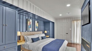 Un dormitorio con una cama grande, una mesita de noche, un aparador y un televisor montado en la pared.