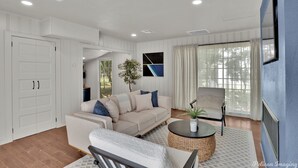 Una sala de estar moderna con un sofá seccional color beige, una mesa redonda y un televisor montado en una pared azul.