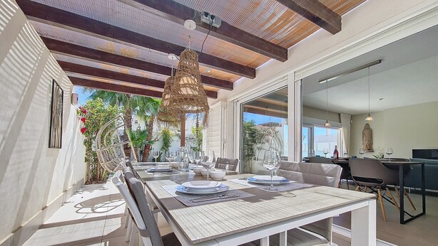 A dining area with a white table set for six, a hanging light fixture, and a view of the outdoors. - Villa with private pool and garden (Mar de Cristal)