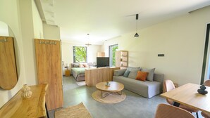 Una sala moderna con sofá, mesa de centro y mesa de comedor. Hay un televisor y un aparador de madera.