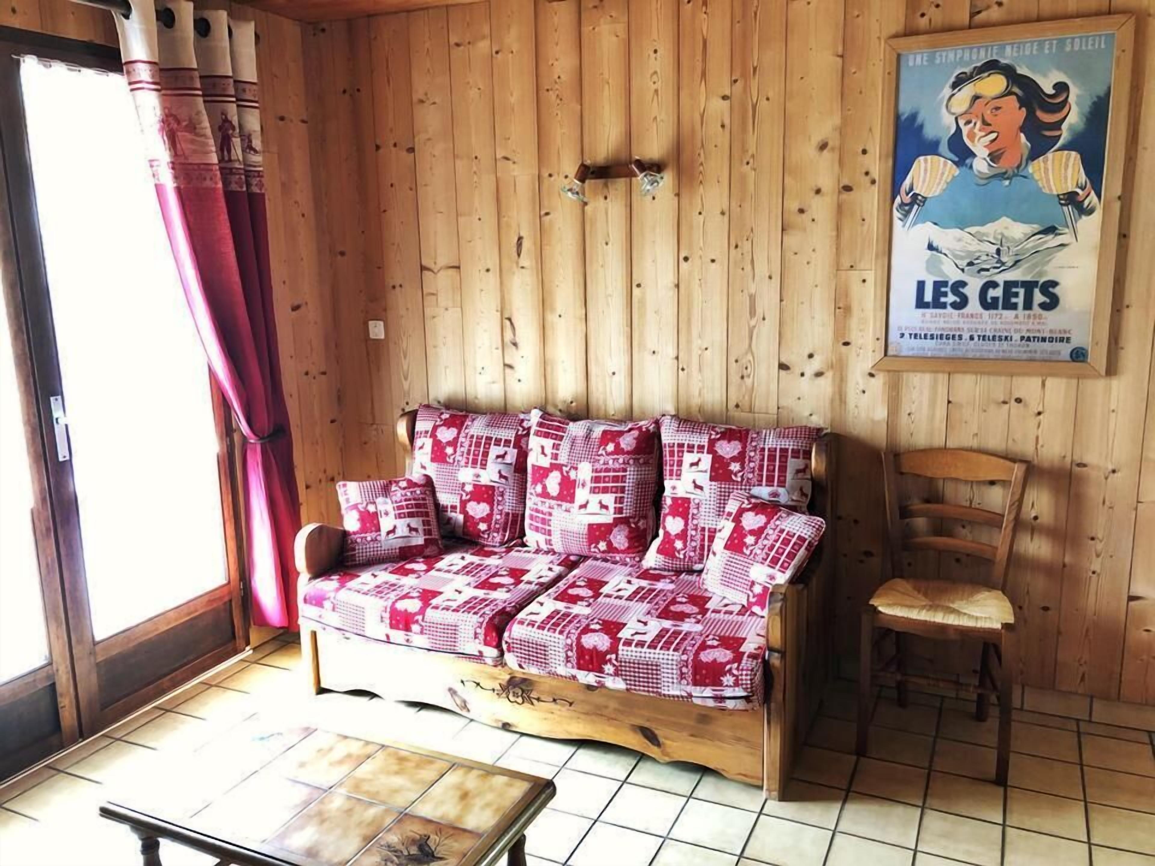 Een houten blokhut van binnen, met een bank, een stoel en een betegelde vloer.