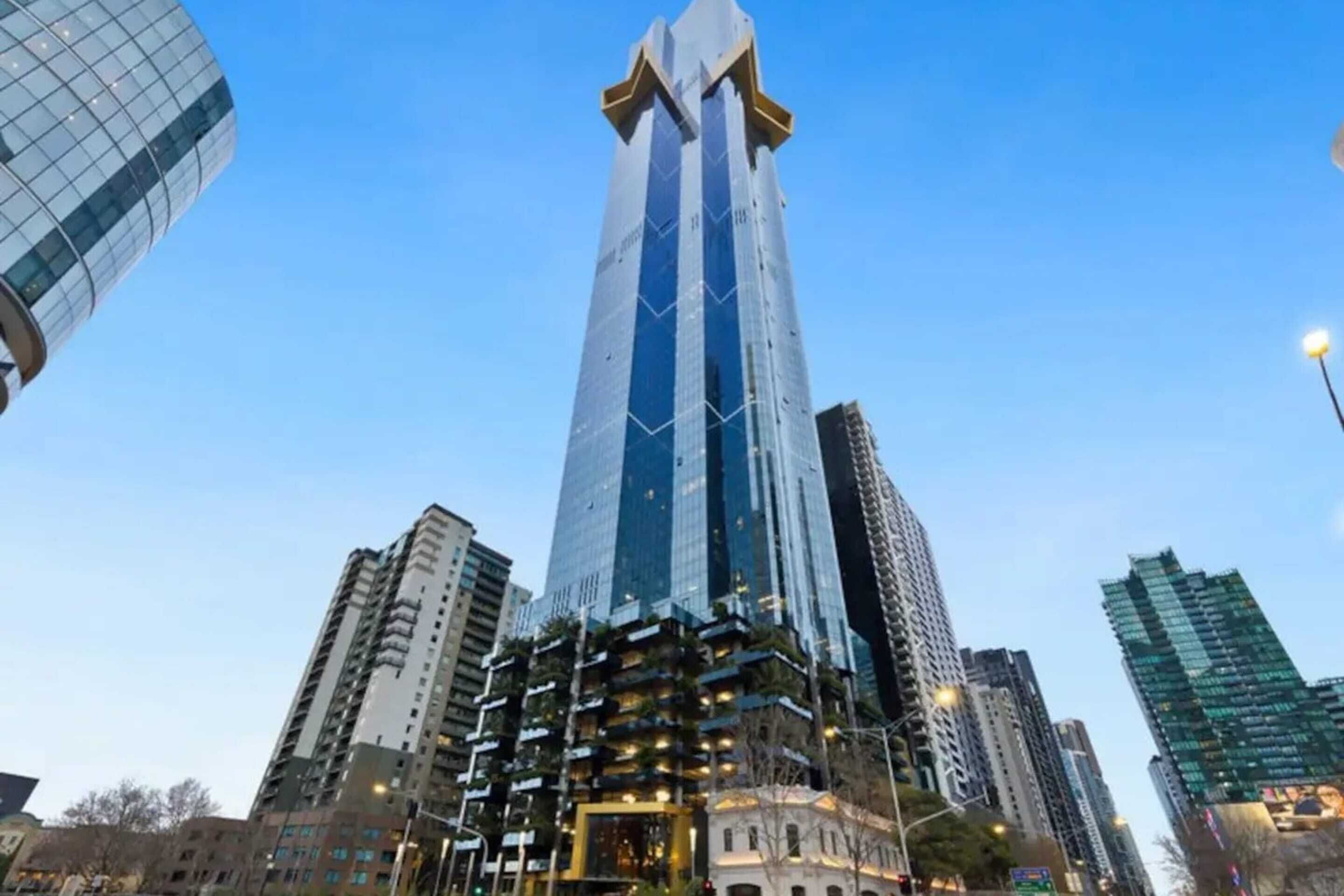 En høj, moderne skyskraber med et unikt arkitektonisk design, omgivet af andre høje bygninger.