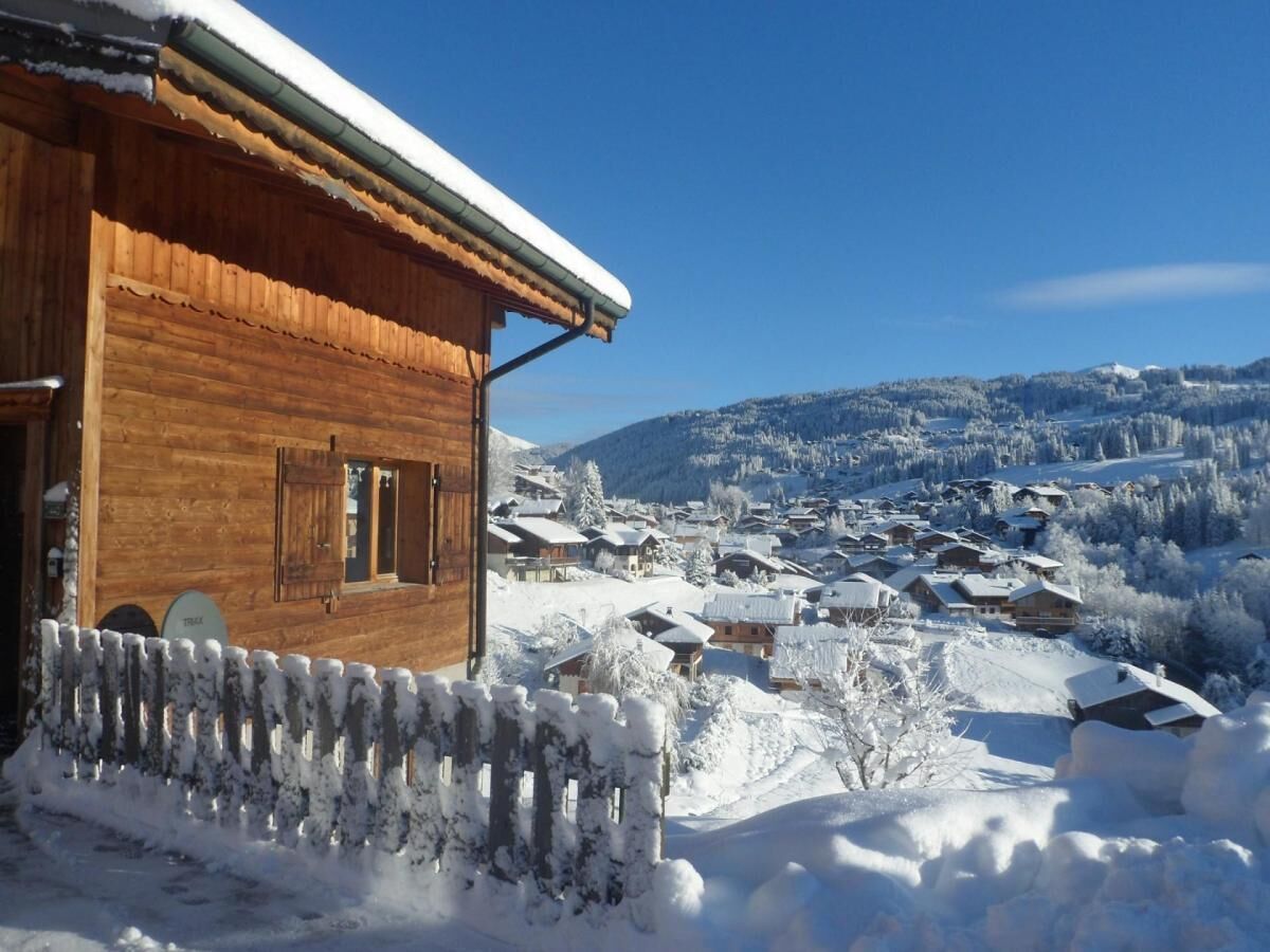 A wooden cabin with a snow-covered roof and a wooden fence in front.