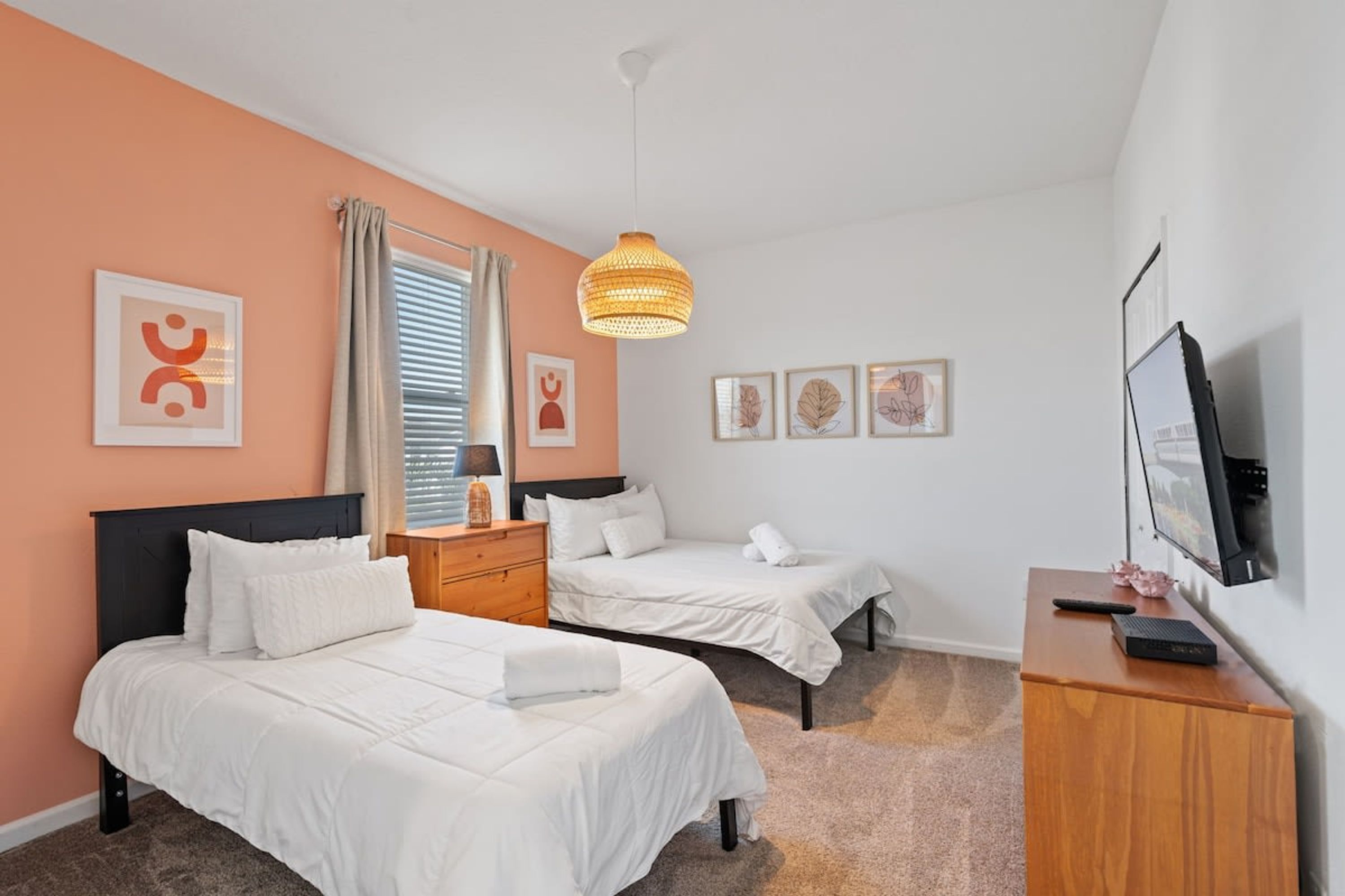 A hotel room with two beds, a wooden dresser, a television, and artwork on the walls.