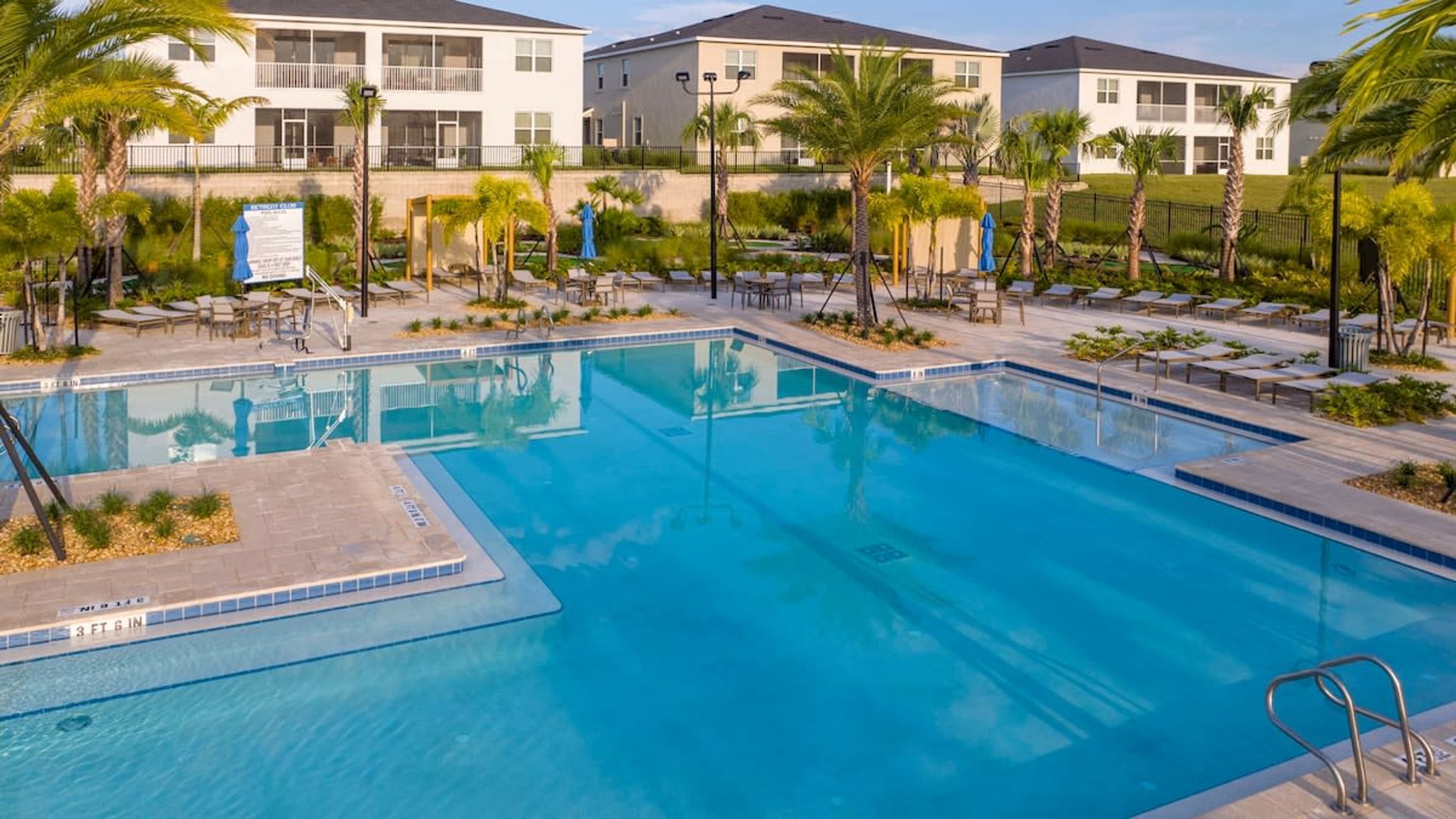 A rectangular pool with clear blue water, surrounded by lounge chairs and palm trees.