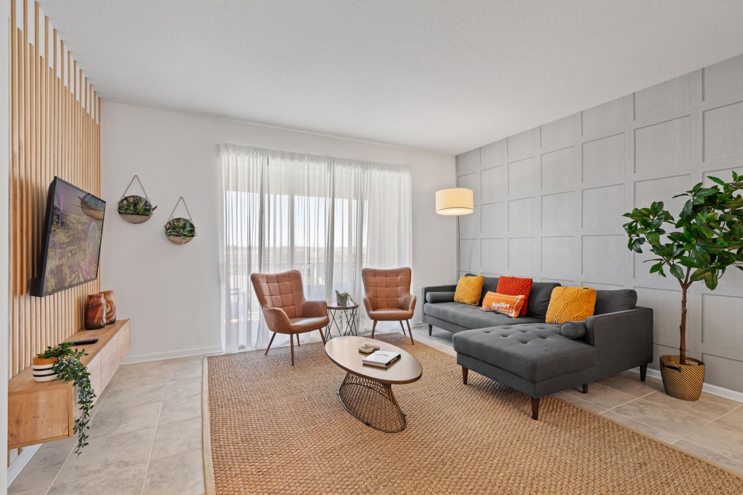 Ein modernes Wohnzimmer mit einem grauen Sofa, zwei Sesseln, einem Couchtisch und einem großen Fenster mit durchsichtigen Vorhängen.
