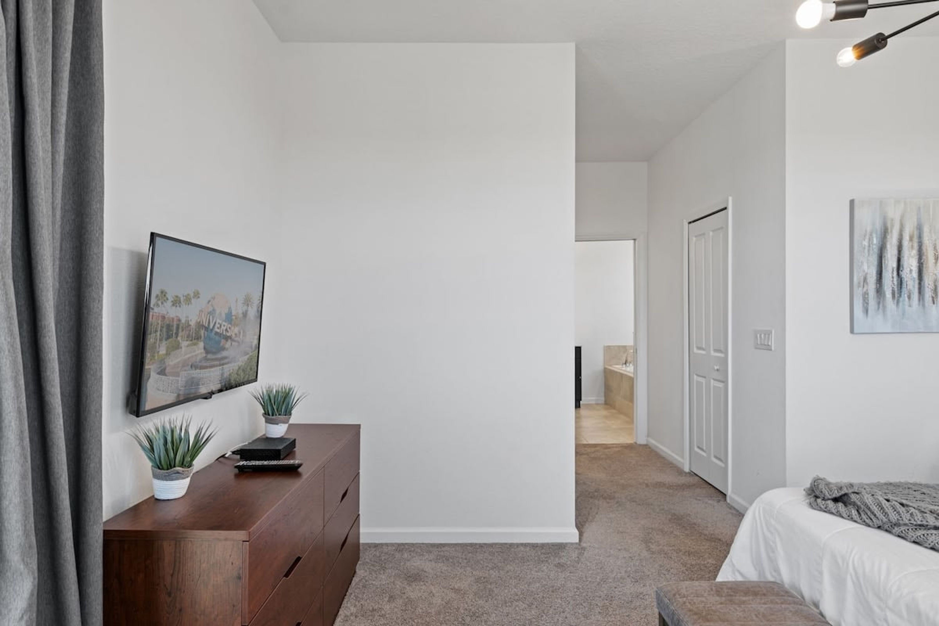 A bedroom with a bed, a dresser, a painting, and a door leading to another room.