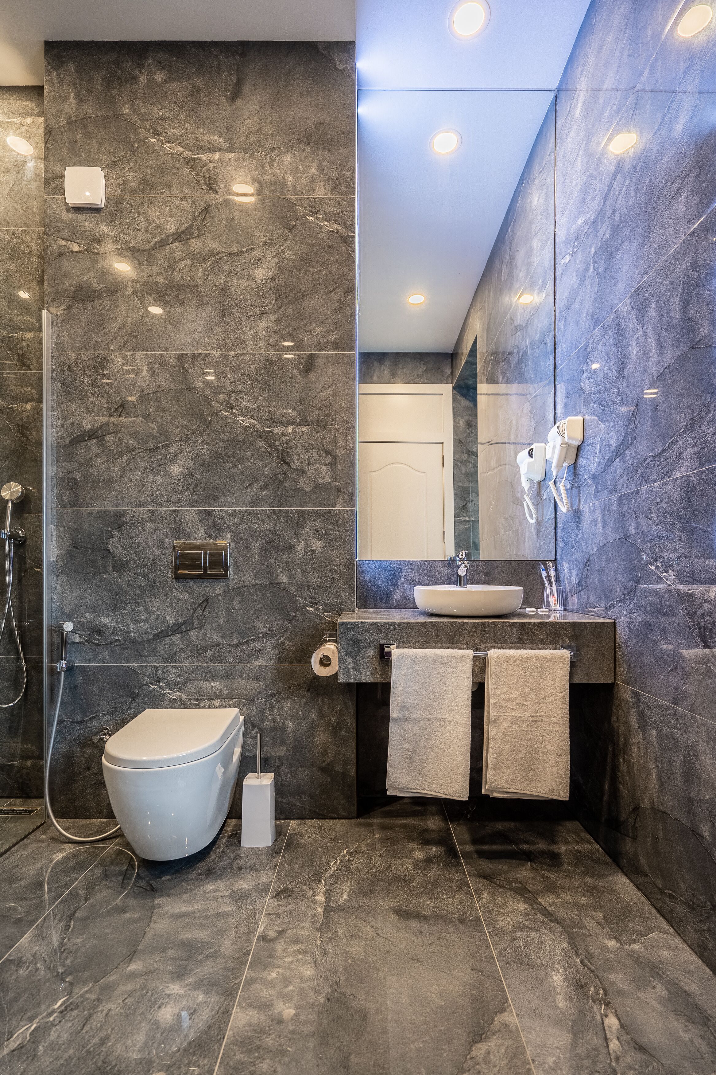 A modern bathroom with a marble wall, a toilet, a sink, and a mirror.