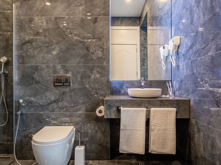 A modern bathroom with a marble wall, a toilet, a sink, and a mirror.