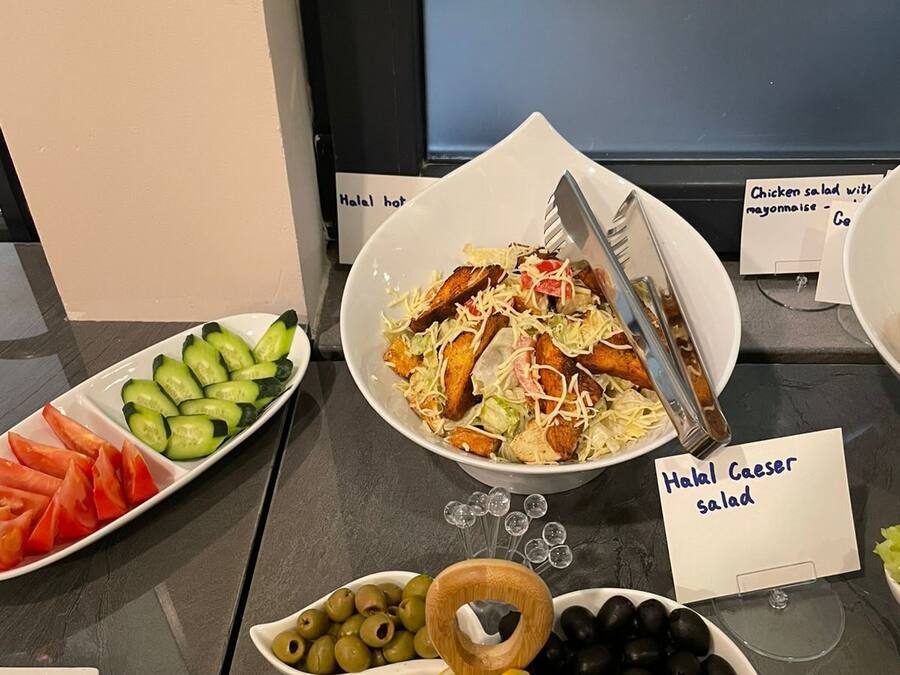 A buffet table with various dishes including a salad, tomatoes, cucumbers, and olives.