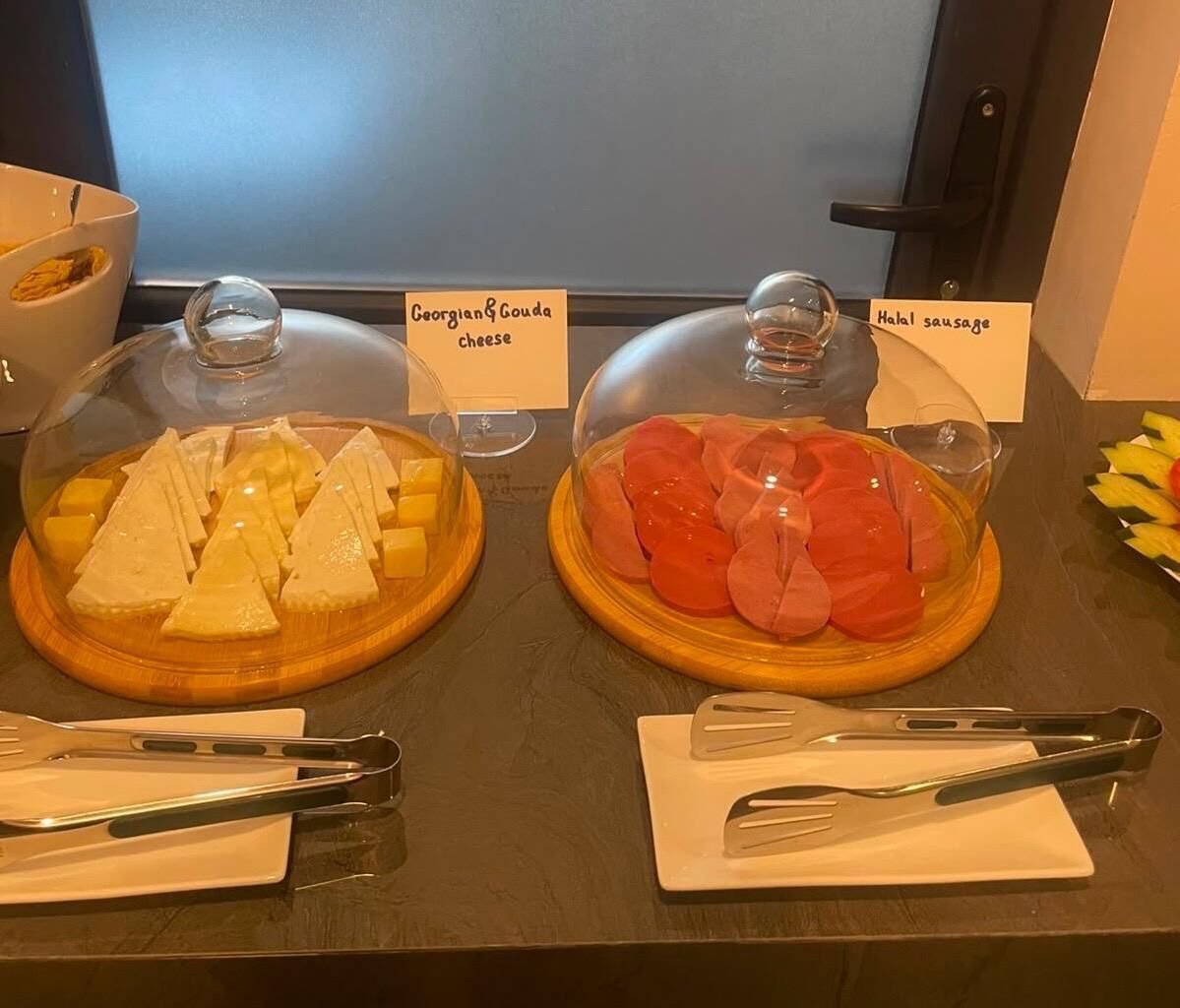 Un bufé con queso Gouda georgiano y salchicha halal bajo campanas de cristal.