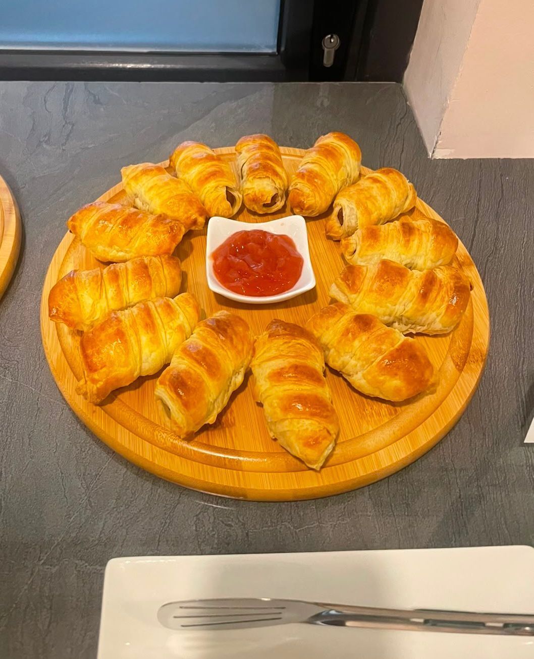 Een ronde houten plank met goudbruine gebakjes en een kleine schaaltje rode saus.