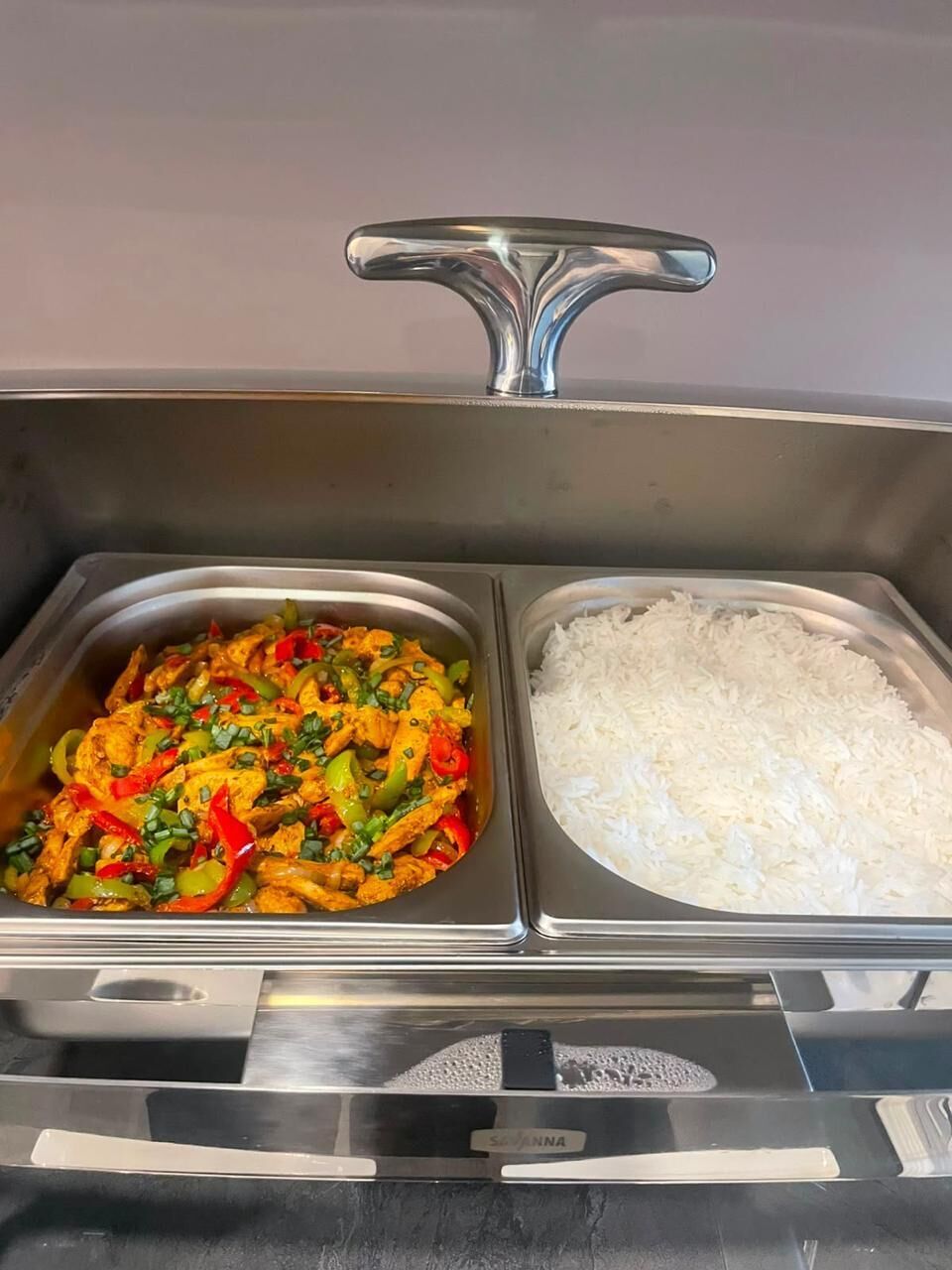 Ein Buffet mit zwei Metalltabletts, auf dem eine Hähnchenspeise mit Gemüse und auf dem anderen weißer Reis serviert werden.